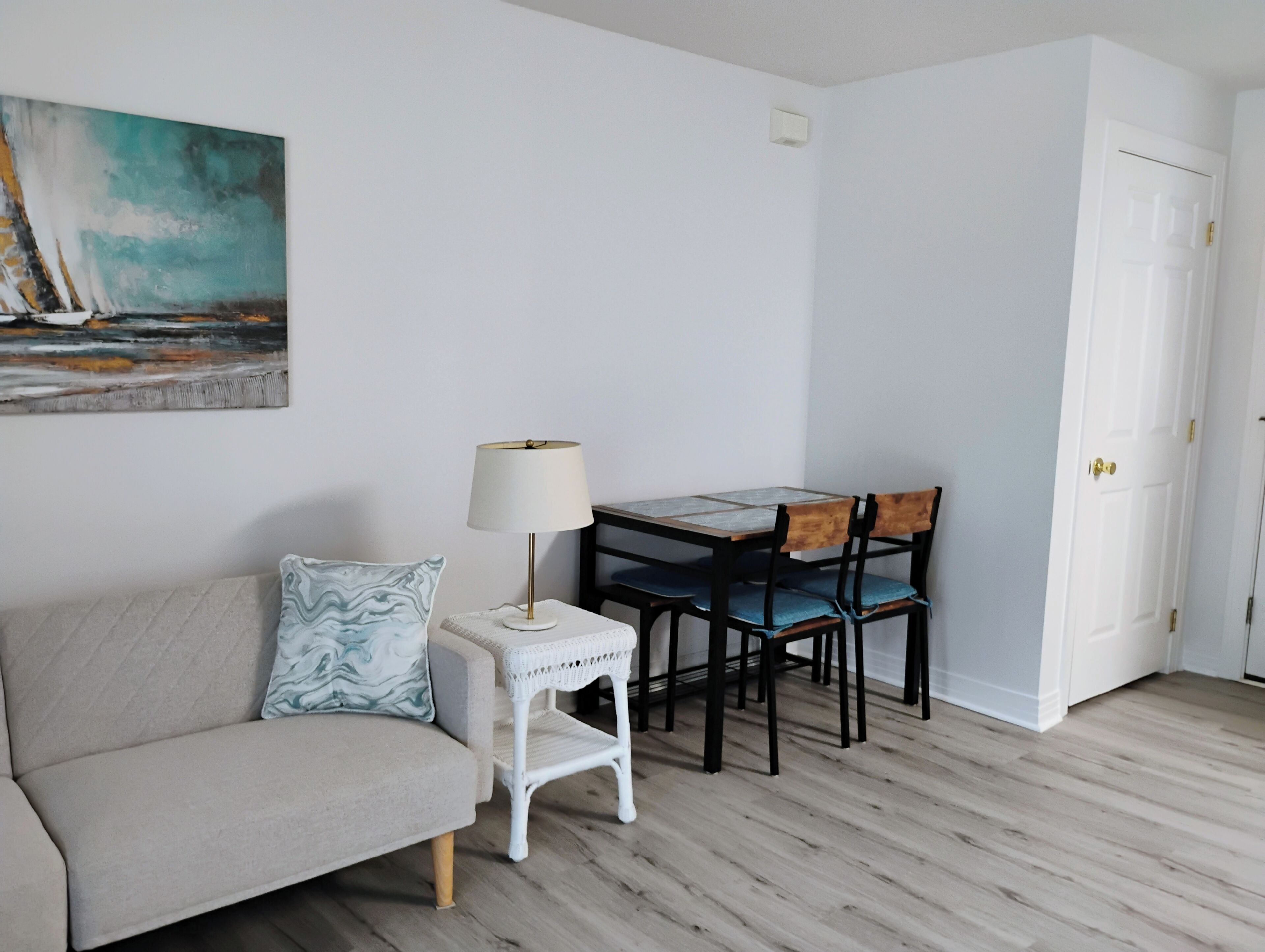 A room with a sofa, a small table with a lamp, and a dining table with chairs.