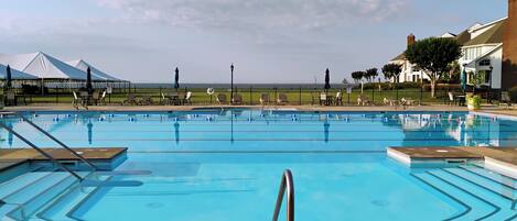 A swimming pool with a view of the ocean, surrounded by lounge chairs and umbrellas.