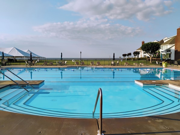 A swimming pool with a view of the ocean, surrounded by lounge chairs and umbrellas.