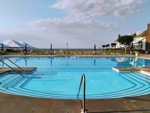 A swimming pool with a view of the ocean, surrounded by lounge chairs and umbrellas.