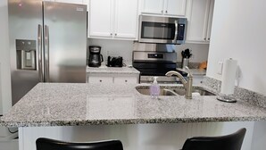 A modern kitchen with white cabinets, stainless steel appliances, a granite countertop, and two black bar stools.