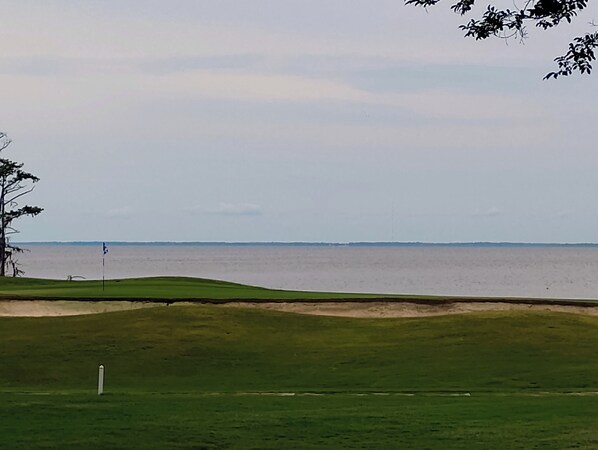 Un campo da golf con una bandierina, uno specchio d'acqua sullo sfondo e un cielo sereno.