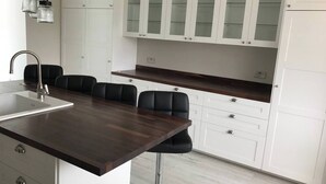 Moderni keittiö, jossa on tumma puinen keittiösaareke, valkoiset kaapit ja mustat baarituolit.