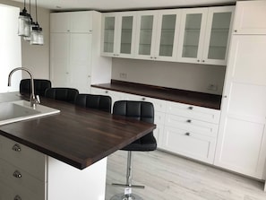 Moderni keittiö, jossa on tumma puinen keittiösaareke, valkoiset kaapit ja mustat baarituolit.
