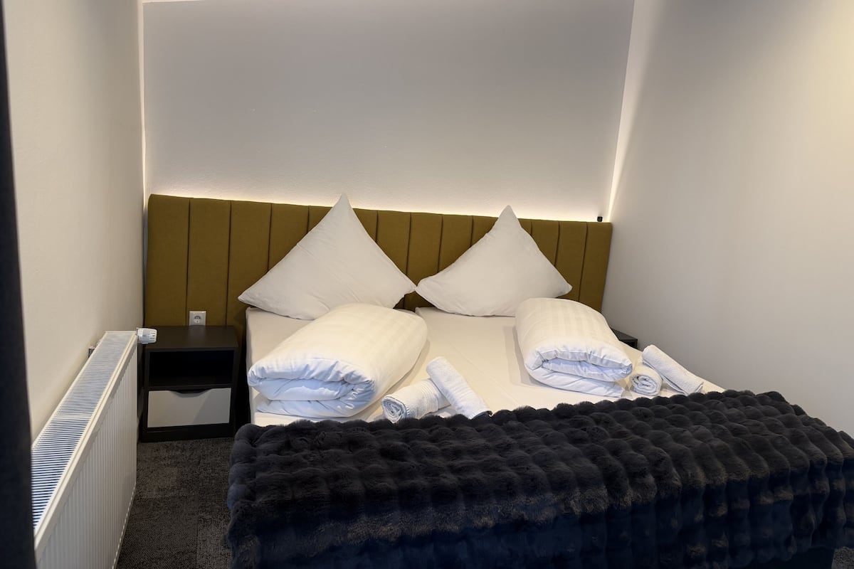 Una habitación de hotel con cama, cabecera, mesita de noche y radiador.