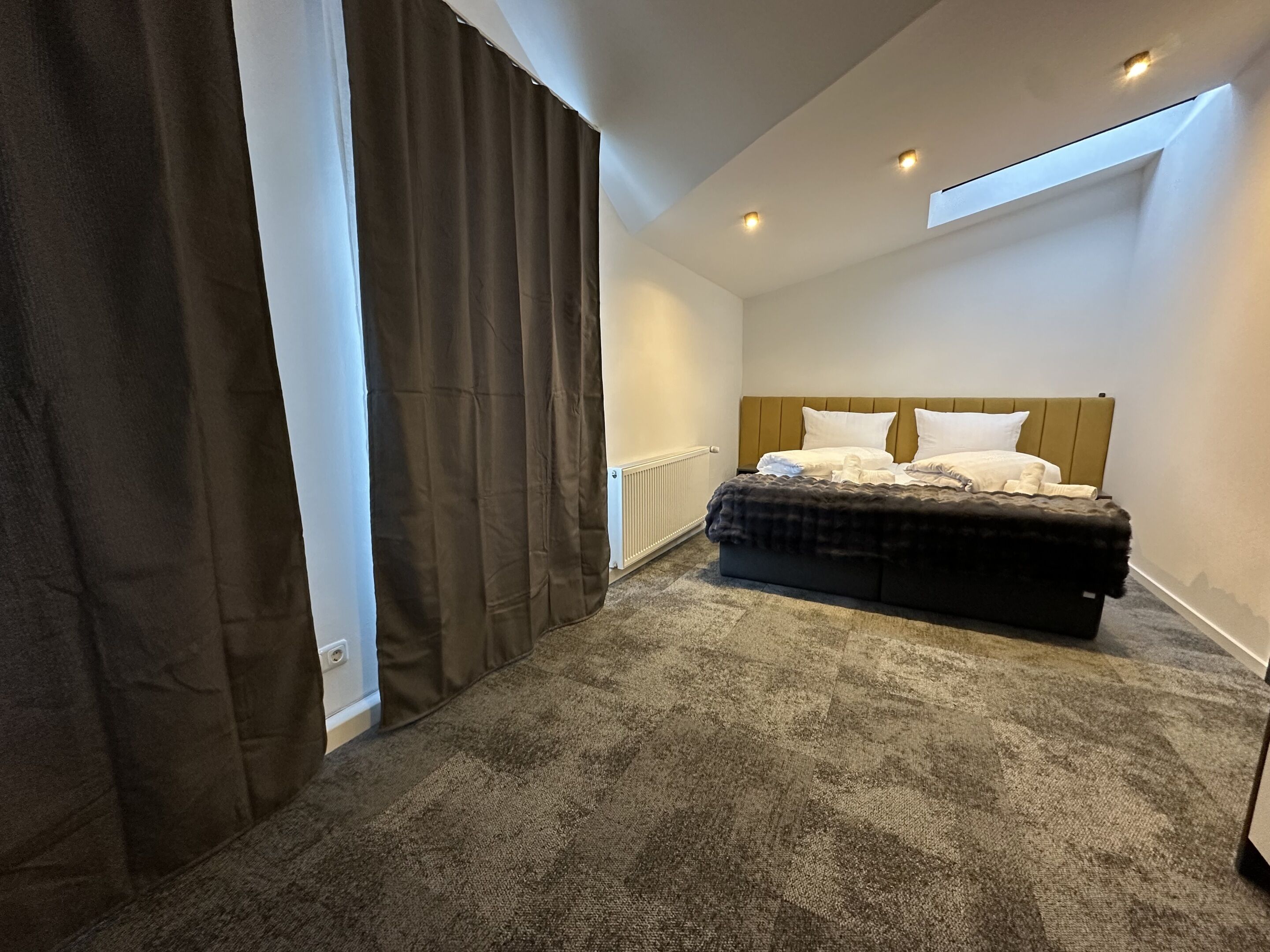 Une chambre à coucher avec un lit, un radiateur, une fenêtre avec des rideaux et un puits de lumière.