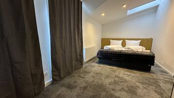 Une chambre à coucher avec un lit, un radiateur, une fenêtre avec des rideaux et un puits de lumière.