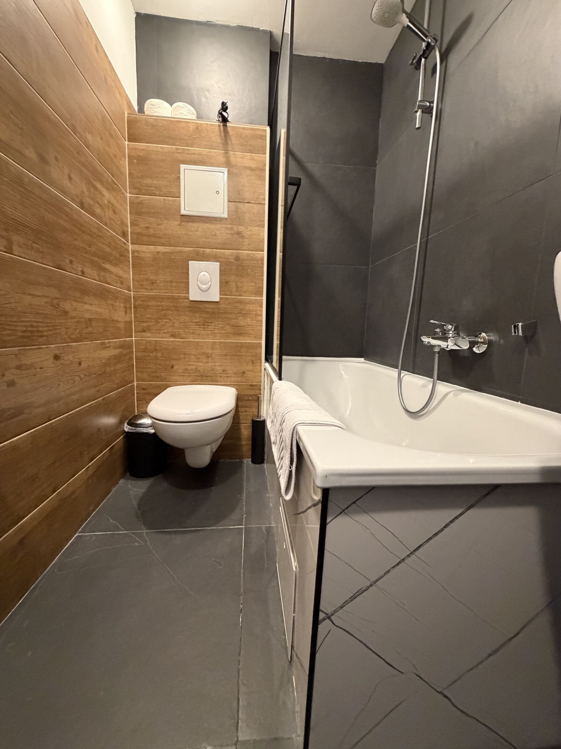 Une salle de bain moderne avec un meuble-lavabo en bois, des toilettes blanches, une baignoire et un espace douche.