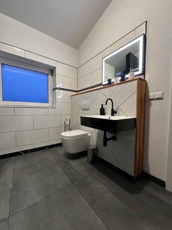 A modern bathroom with a toilet, sink, mirror, and window.