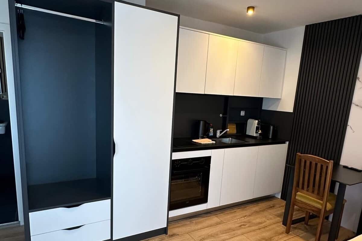 Una cocina compacta con armarios blancos, piso de madera y una sola silla.