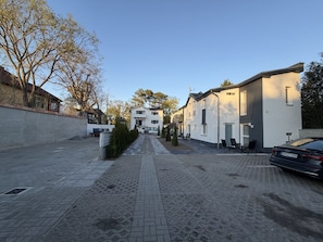 A residential street with houses, a paved walkway, and parked cars.
