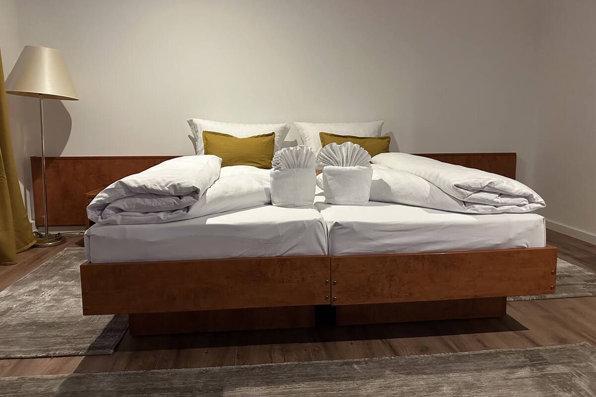 Una cama bien hecha con sábanas blancas, un cabecero de madera y una lámpara de noche.