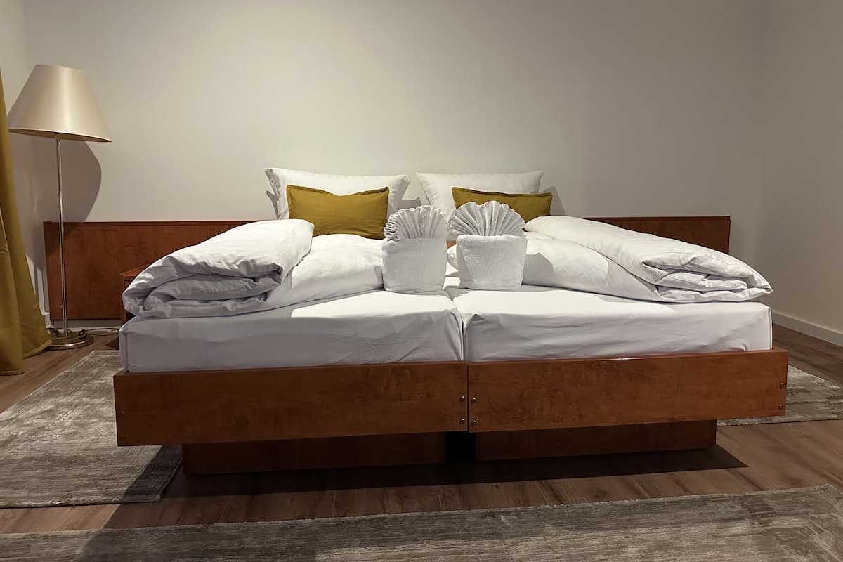 Un letto rifatto con lenzuola bianche, una testiera in legno e una lampada da comodino.