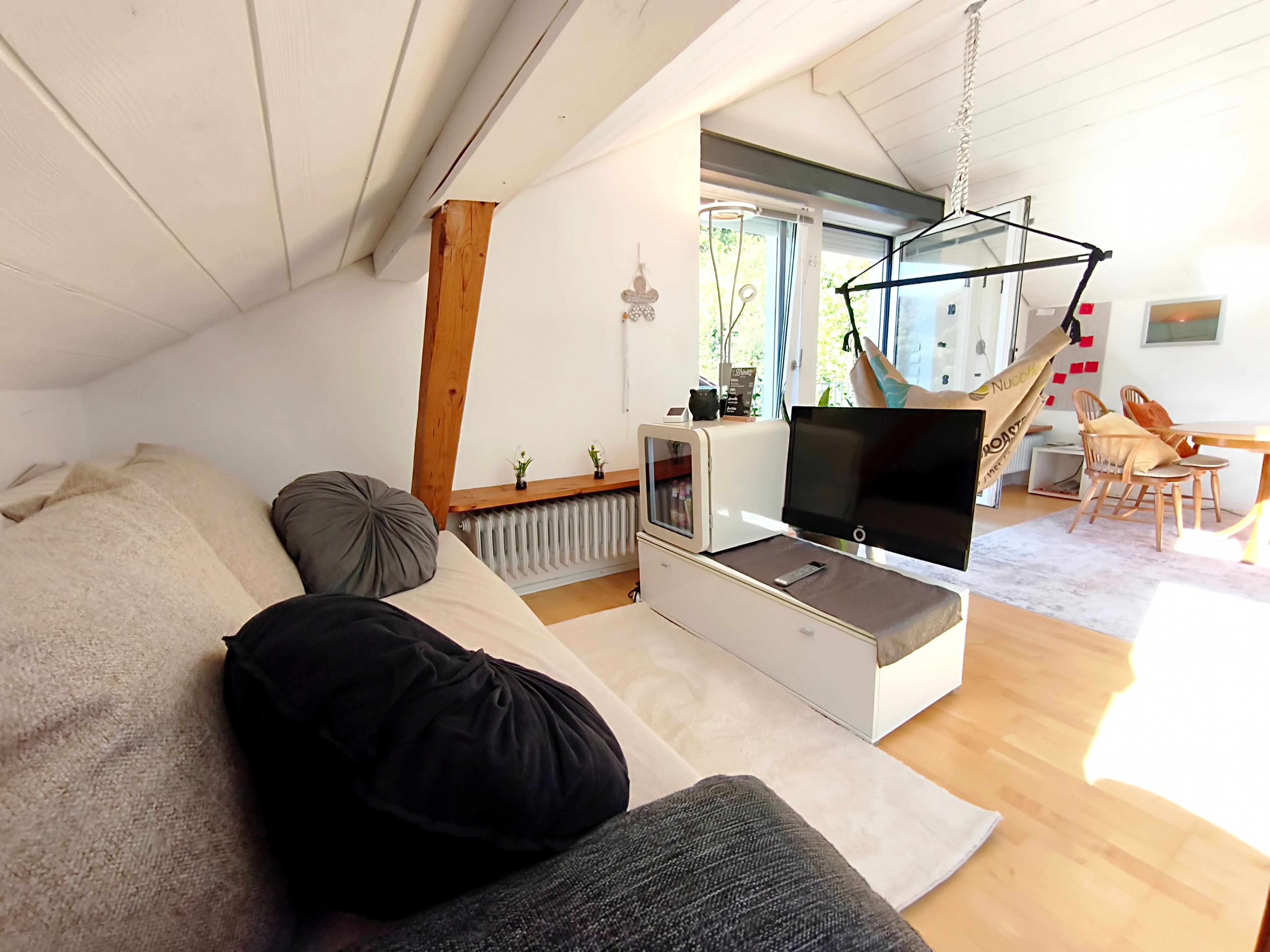 Ett modernt vardagsrum med en soffa, en tv, en hängstol och en matplats med stolar och ett bord.