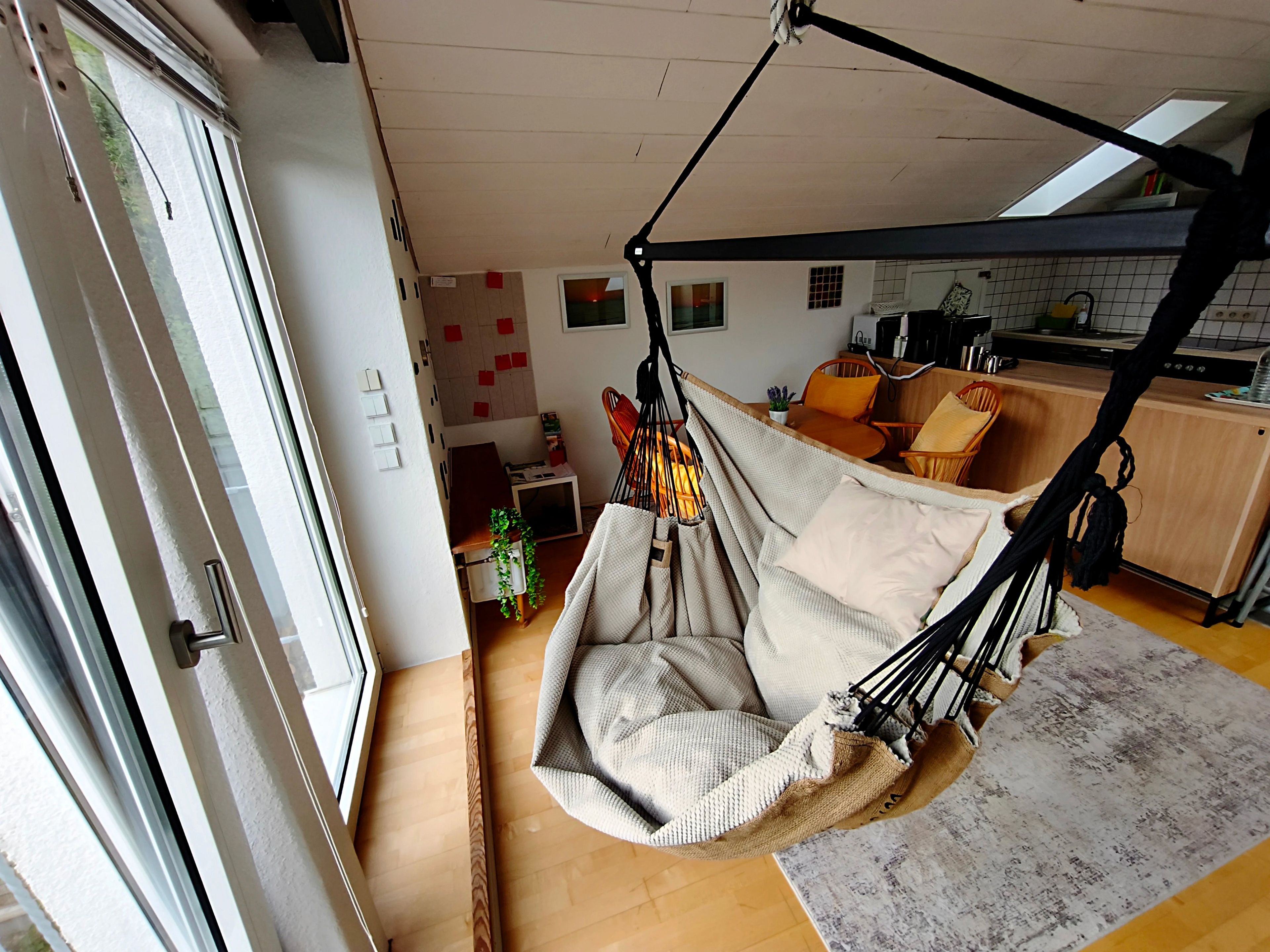 A room with a hanging chair, a kitchen area, and a dining table with chairs.