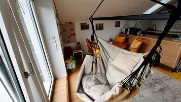 A room with a hanging chair, a kitchen area, and a dining table with chairs.