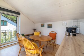 Een eetruimte met een ronde tafel, houten stoelen, een klok aan de muur, en een keuken met apparatuur.