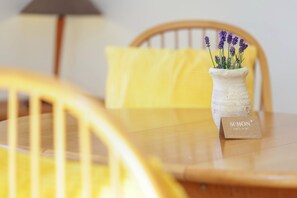 Una mesa con un jarrón de cerámica blanca que contiene flores de lavanda y una tarjeta con la etiqueta 'SCHÖN'.