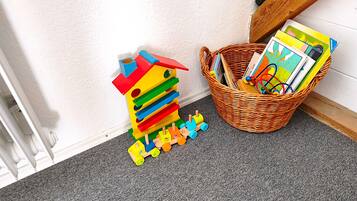 Un coin de pièce avec un mur blanc, une moquette grise, un plancher en bois et un panier en osier rempli de livres et de jouets.