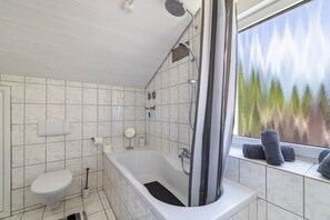 Een badkamer met een bad, toilet en raam, handdoeken aanwezig.
