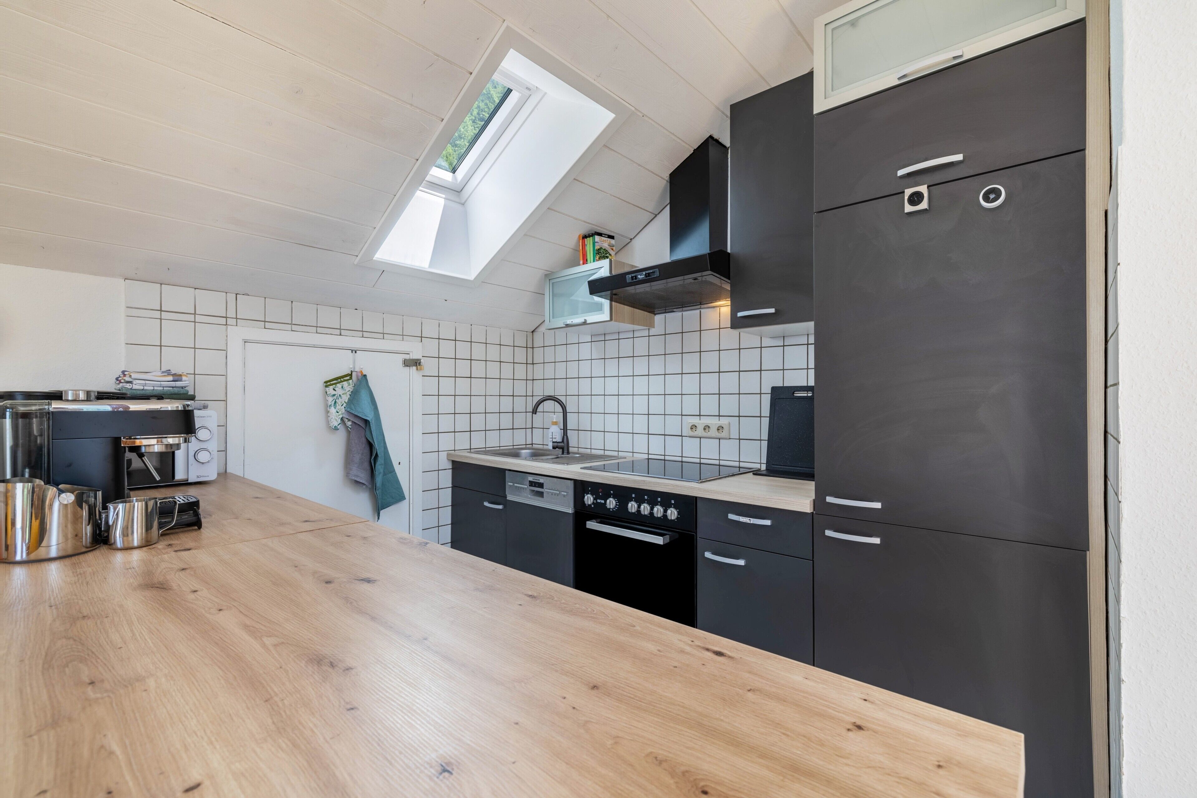 A modern kitchen with a wooden countertop, black cabinets, a built-in oven, and a skylight.
