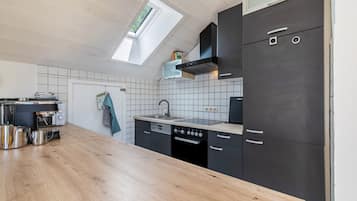 A modern kitchen with a wooden countertop, black cabinets, a built-in oven, and a skylight.
