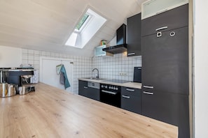 A modern kitchen with a wooden countertop, black cabinets, a built-in oven, and a skylight.