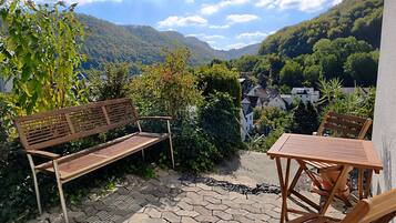 Un patio con un banco y una mesa de madera, rodeado de follaje y vistas a un valle.