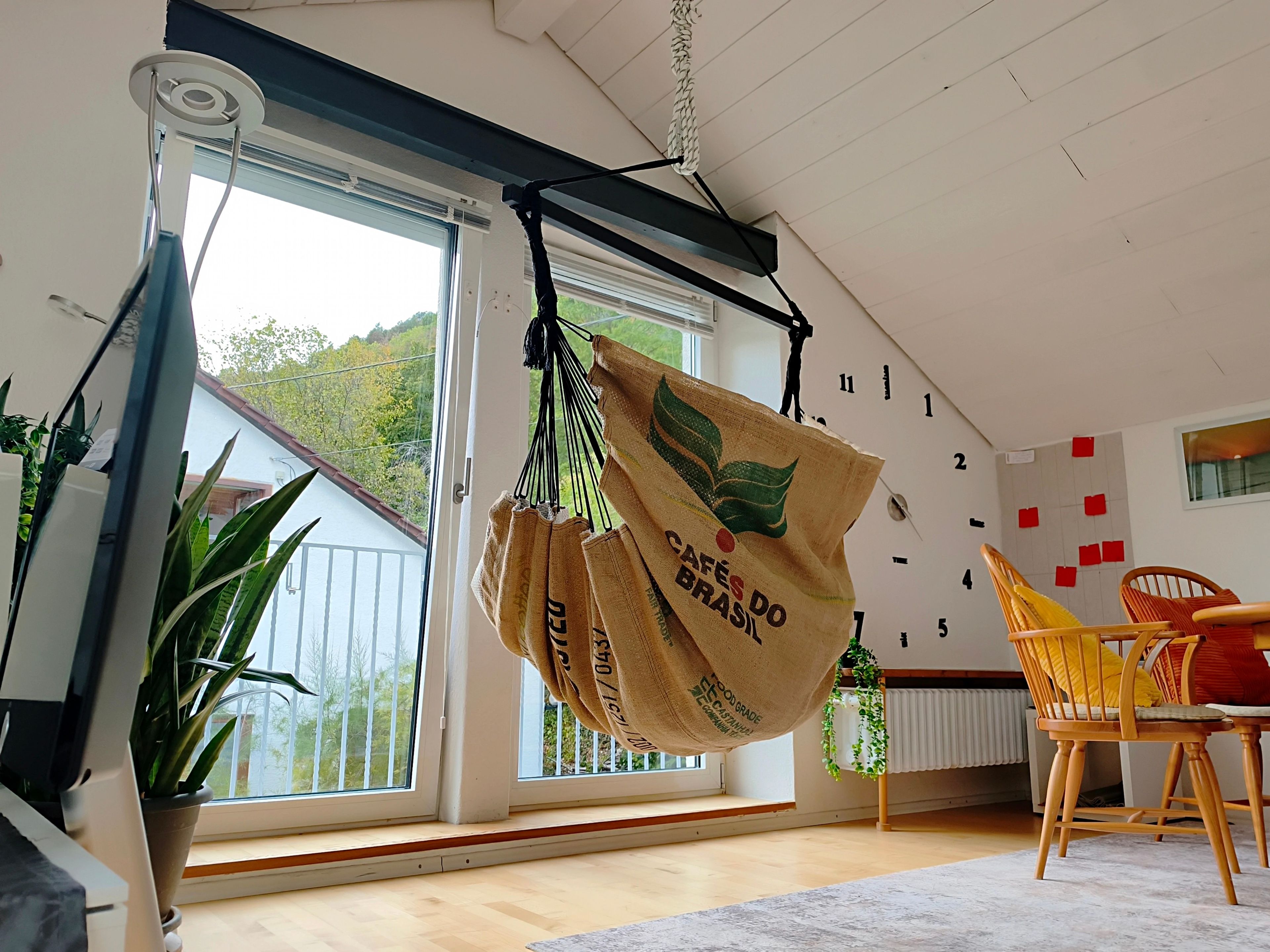 A room with a hanging bag, a window with a view of greenery, a chair, and a wall with numbers.