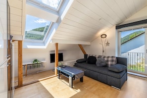 A modern loft-style room with a sloped ceiling, skylights, a sofa, a coffee table, and a radiator.