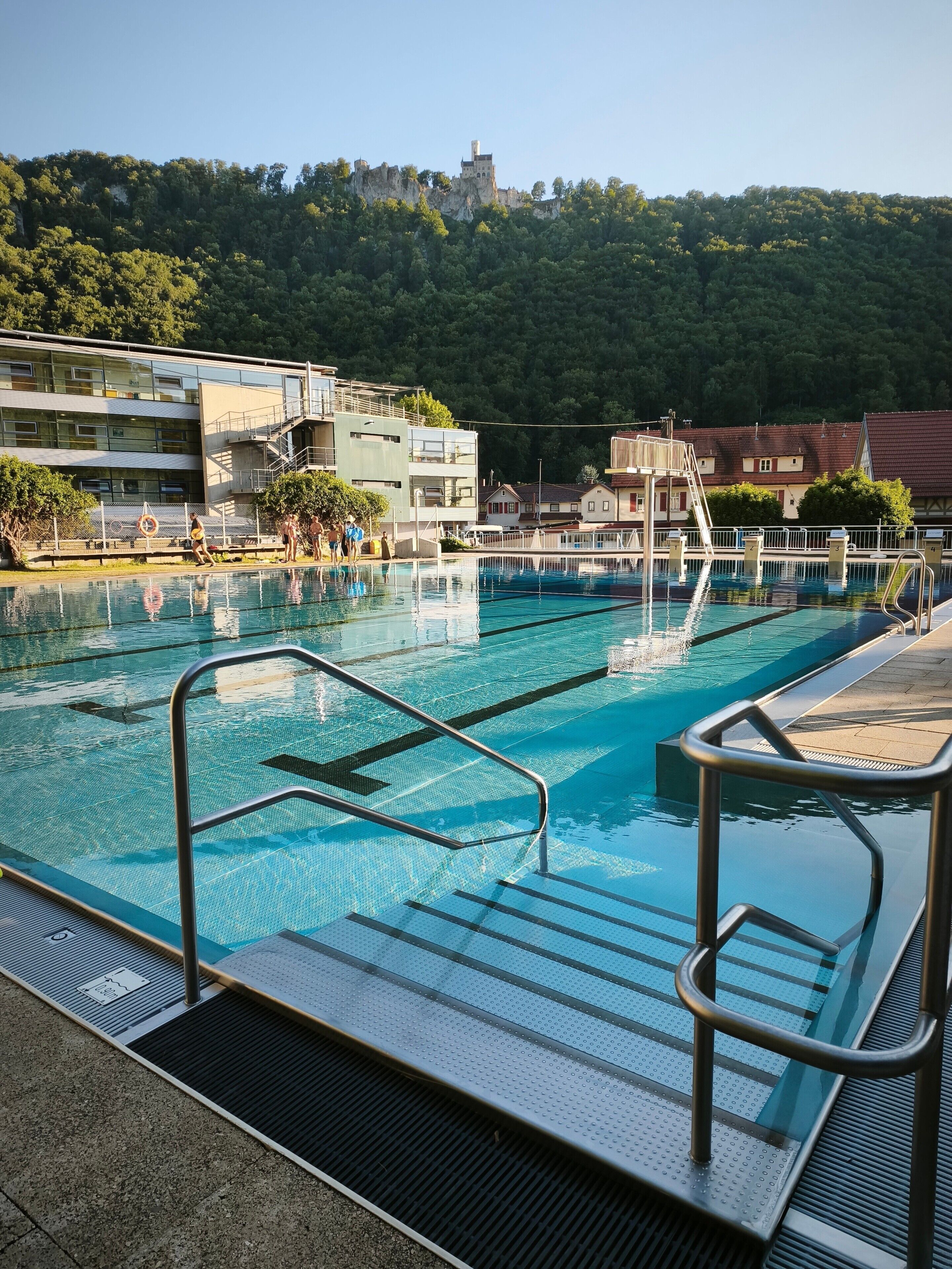 Ein Schwimmbecken mit klarem Wasser, Metallgeländern und einer gefliesten Liegefläche.