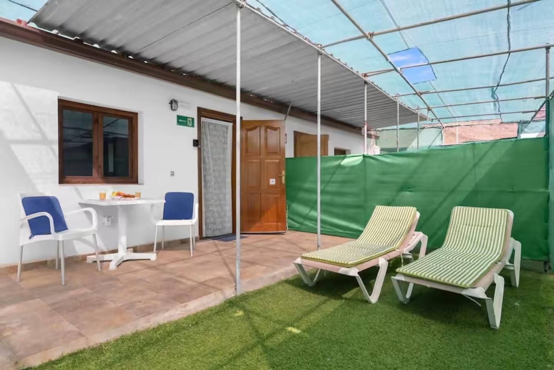Een overdekt buitengebied met terras, twee lounge fauteuils en een tafel met stoelen.
