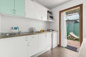 A kitchen with white cabinets, a stainless steel sink, and a microwave. There is a window with a view of a green area outside. - Country Studio Near Fataga (San Bartolomé de Tirajana)