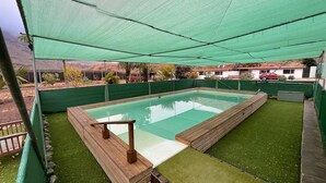 A rectangular swimming pool with a wooden deck, surrounded by green artificial grass, under a green canopy. - Country Studio Near Fataga (San Bartolomé de Tirajana)