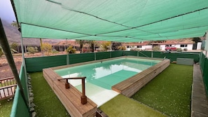 A rectangular swimming pool with a wooden deck, surrounded by green artificial grass, under a green canopy. - Country Studio Near Fataga (San Bartolomé de Tirajana)