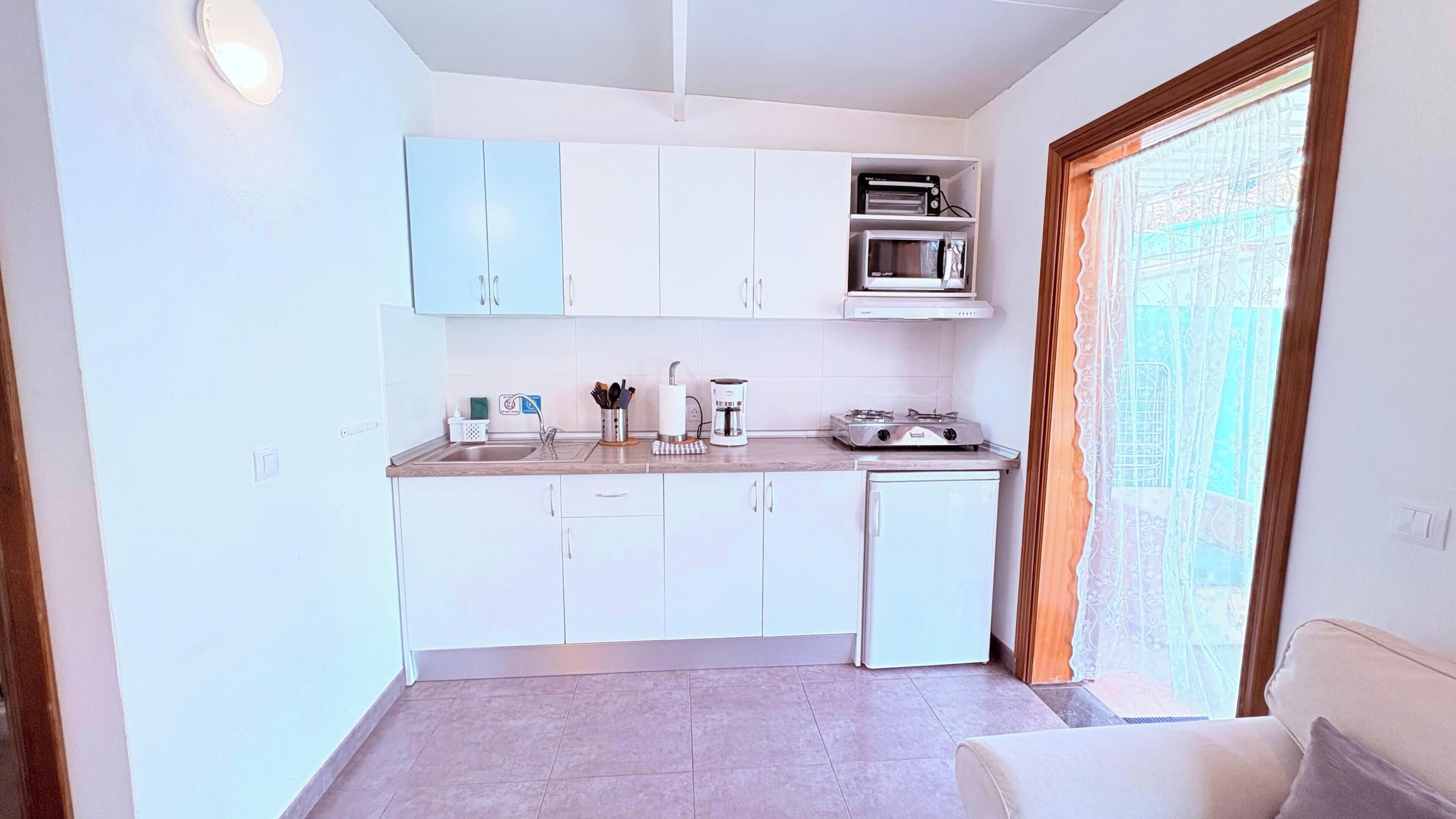 A compact kitchen with white cabinets, a coffee machine, and a small stove.