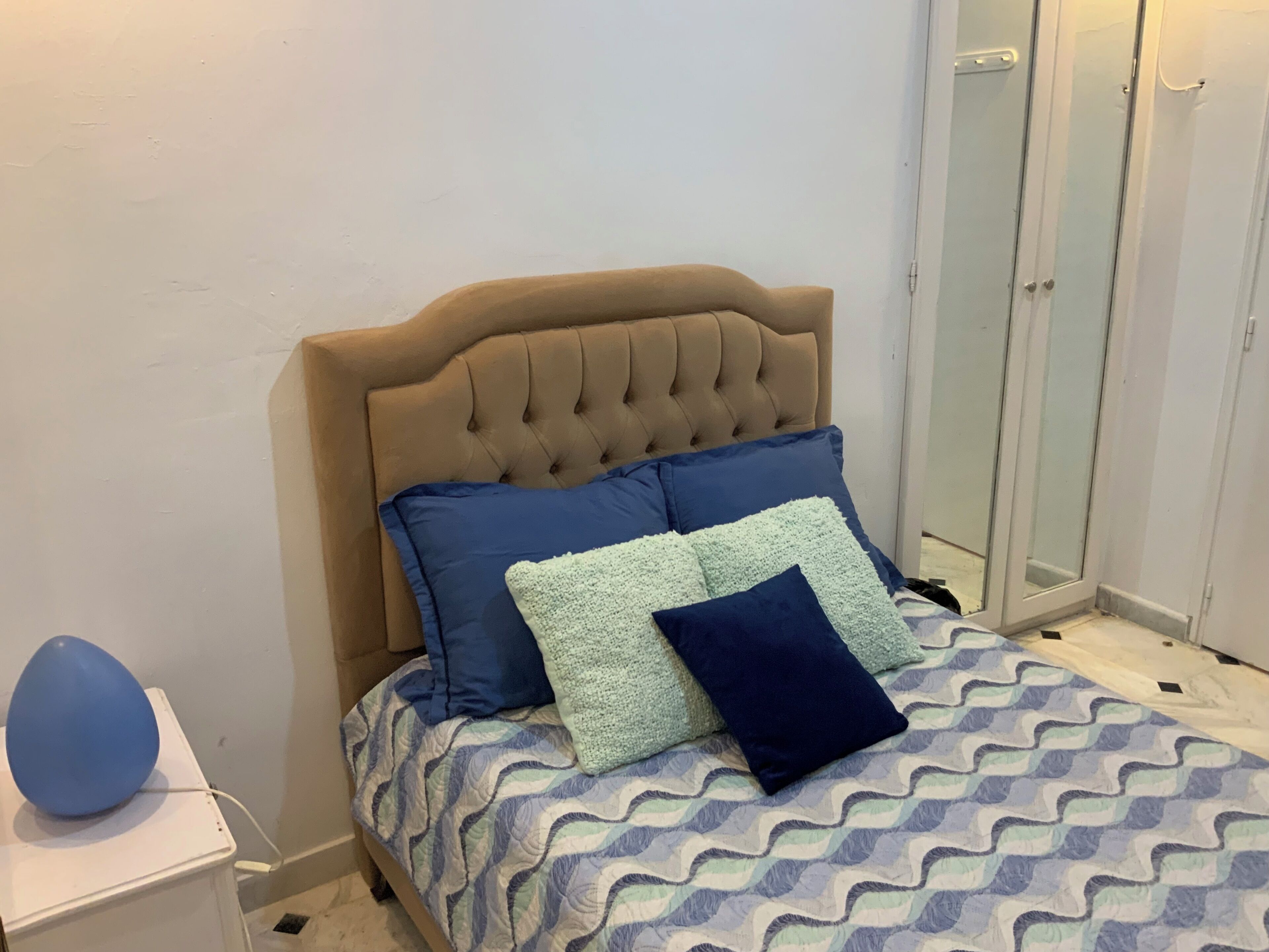 A bed with a tufted headboard, a patterned bedspread, and several pillows.