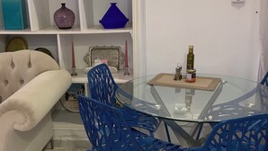 Uma sala de estar com uma mesa de vidro, cadeiras azuis, um sofá branco e prateleiras com objetos decorativos.
