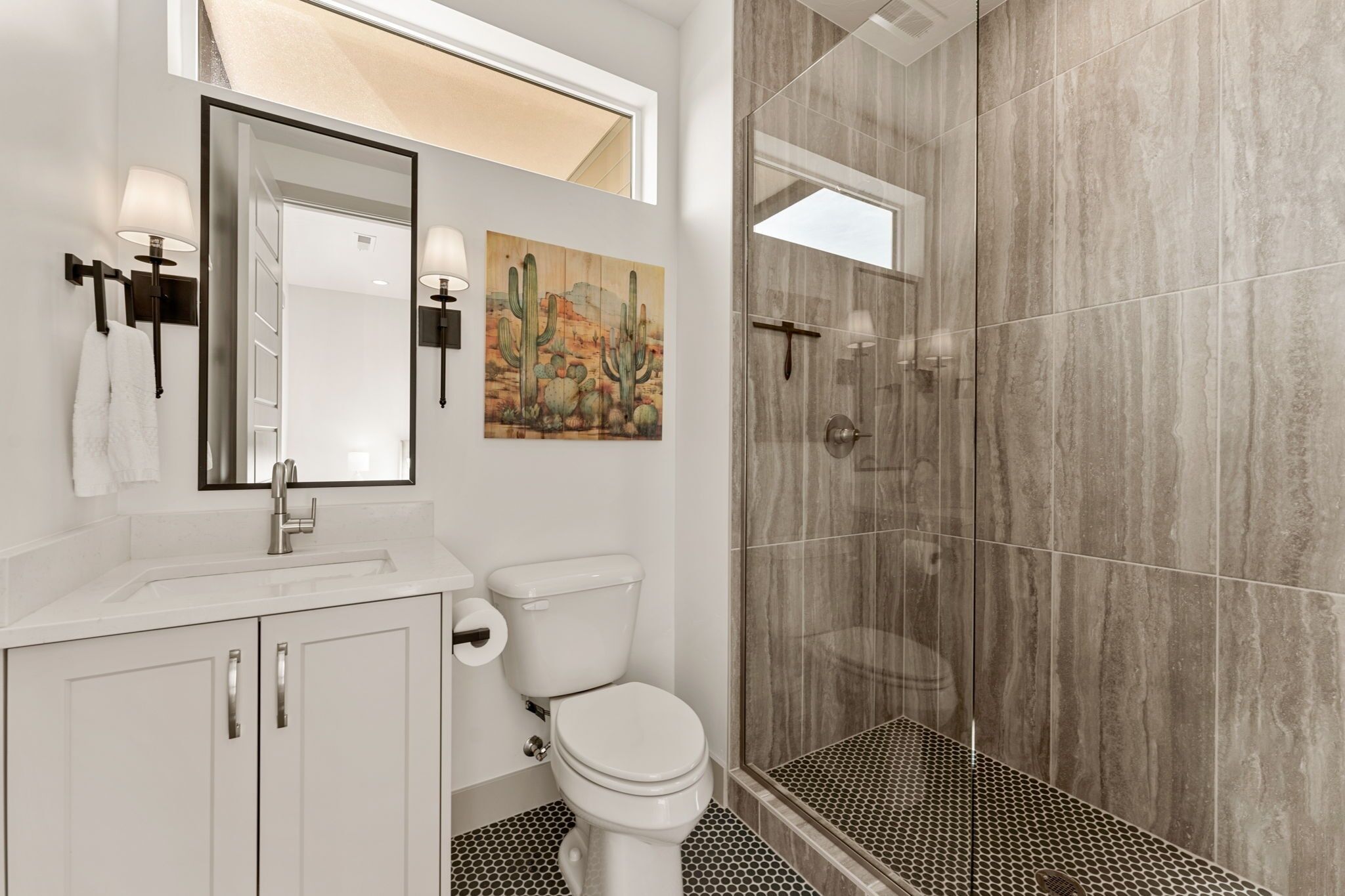 A bathroom with a white sink, a toilet, a shower with glass doors, and a mirror with a painting above it.