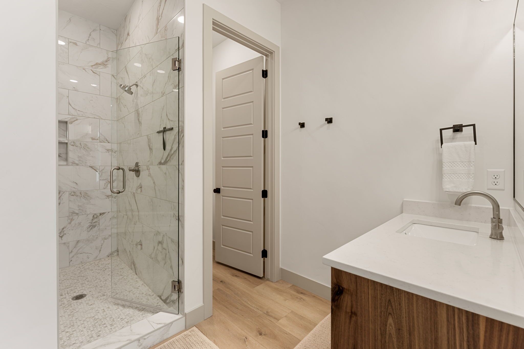 A modern bathroom with a glass-enclosed shower, a wooden vanity, and a white sink.