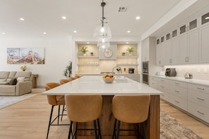 A modern kitchen with a large island, bar stools, and a clock on the wall. - Sunrise Escape 7 Bedroom Home (St. George)