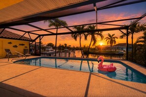 A swimming pool with a pink flamingo float, palm trees, and a sunset view. - Wpw3504 4 Bedroom Home (Punta Gorda)