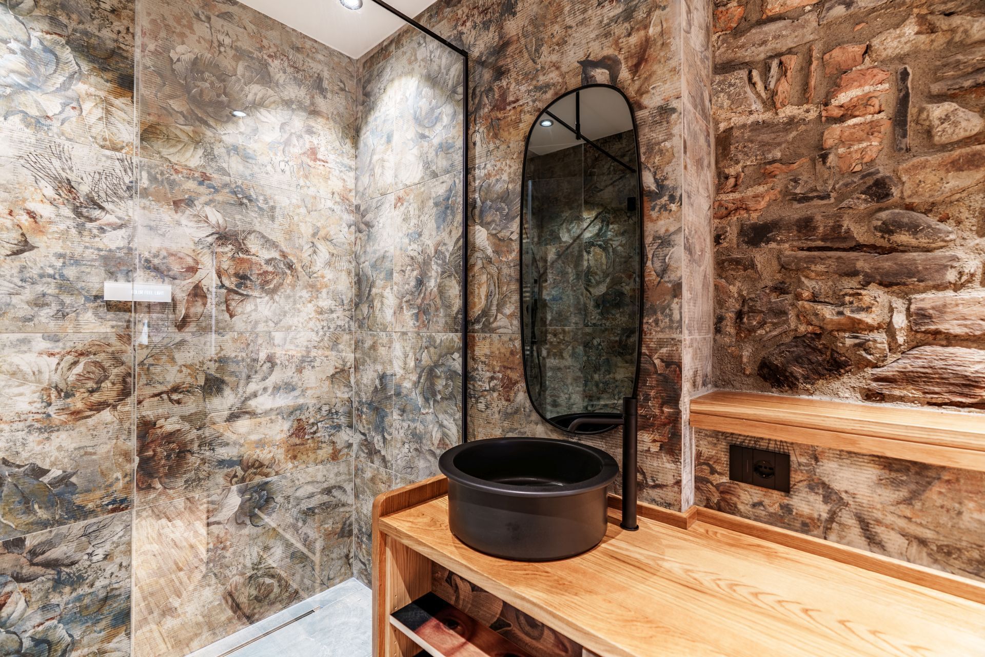 Une salle de bain avec un mur en pierre, un meuble-lavabo en bois et un lavabo noir.