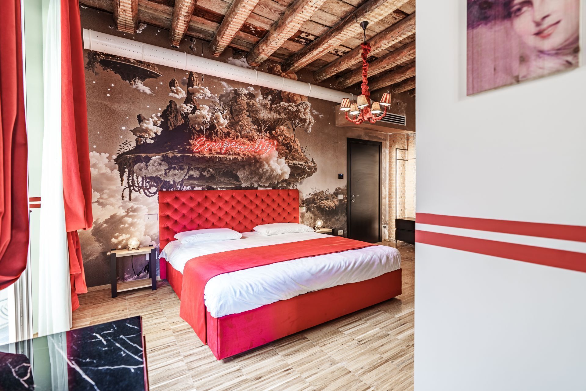 A bedroom with a red bed, a mural on the wall, and a wooden ceiling.