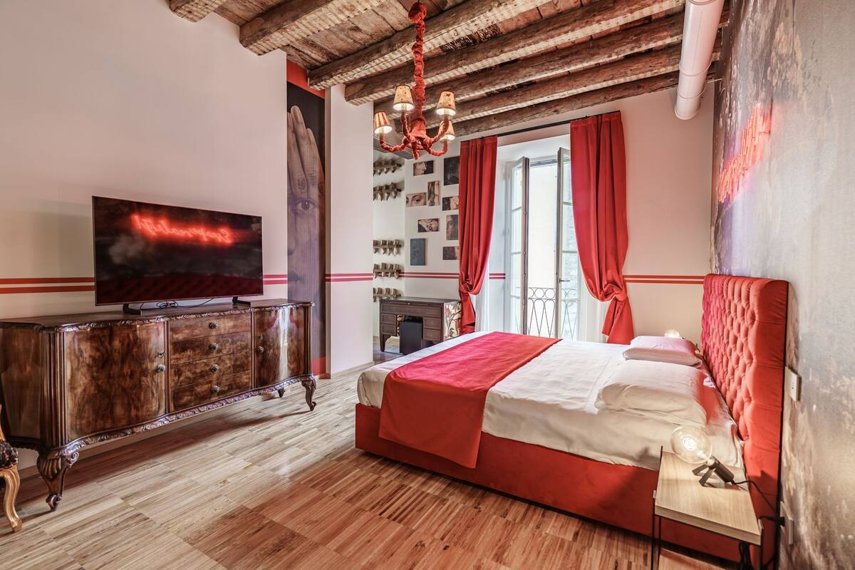Ein Schlafzimmer mit Holzboden, einem Bett mit roter Bettwäsche, einem Fernseher auf einer Holzkommode und einem Kronleuchter.
