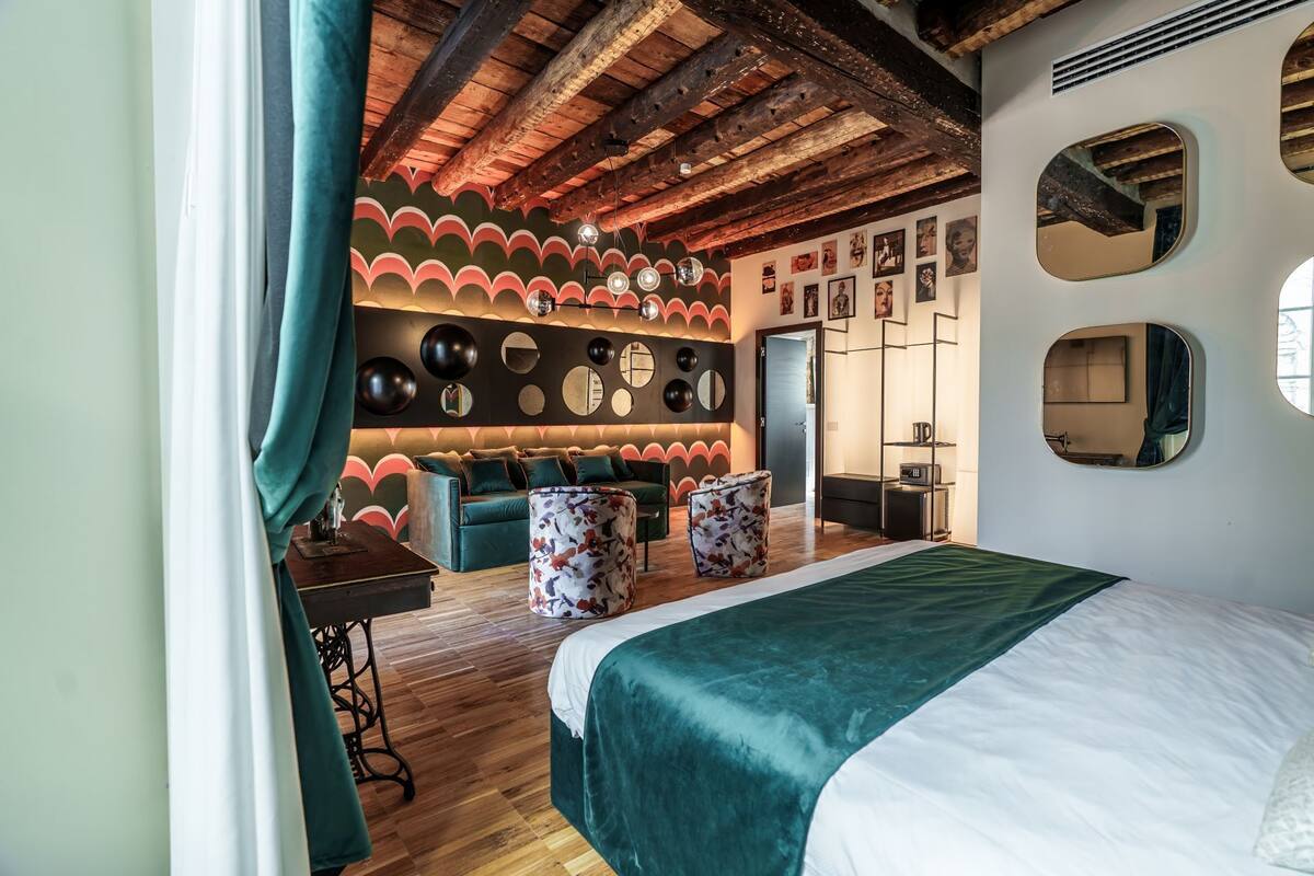 Ein Zimmer mit einem Bett, einem Sofa, einem Couchtisch sowie einer Wand mit runden Spiegeln und Kunstwerken.