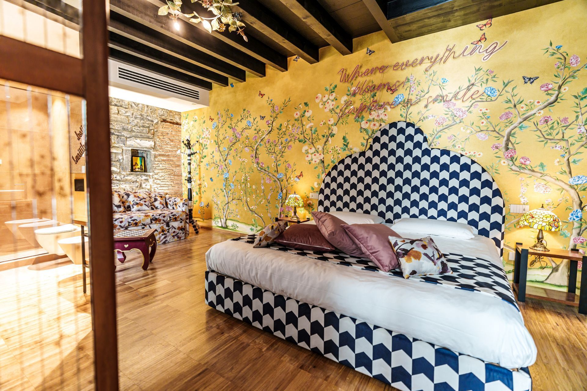 Ein Schlafzimmer mit kariertem Kopfteil, einer Wandmalerei mit Blumenmuster und einem Bett mit geblümter Bettwäsche.