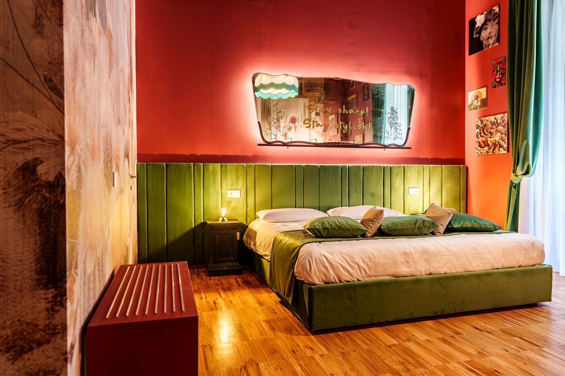Een kamer met een met groen bekleden bed, een nachtkastje met een lamp en een aan de muur bevestigd kunstwerk.