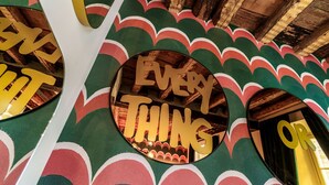 Un miroir rond sur lequel est inscrit le texte « EVERY THING OR », placé sur un mur orné d’un motif ondulé vert et rouge.