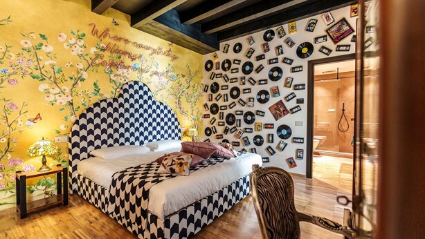 Une chambre avec une tête de lit à carreaux, un papier peint à motifs floraux et un mur recouvert de disques vinyles.